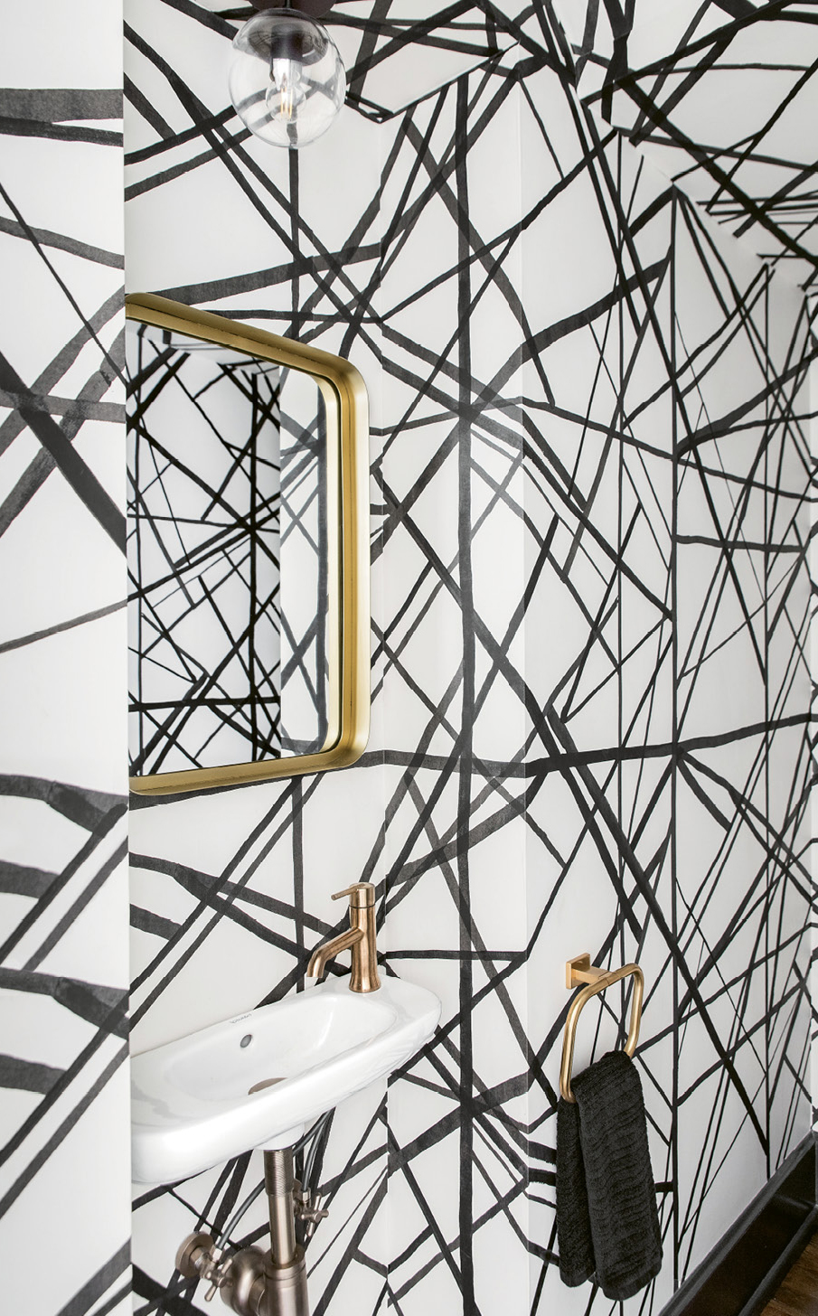 SMALL BUT MIGHTY - “It’s a tiny, under-the-stairs powder room so I knew we had to go big in there,” says Lenox. She covered the walls and ceiling with Kelly Wearstler’s “Channels” wallpaper and painted the door, trim, and casings a glossy black to up the wow factor. A mini sink from Ferguson and gilt mirror from CB2 polish off the practical, petite space.