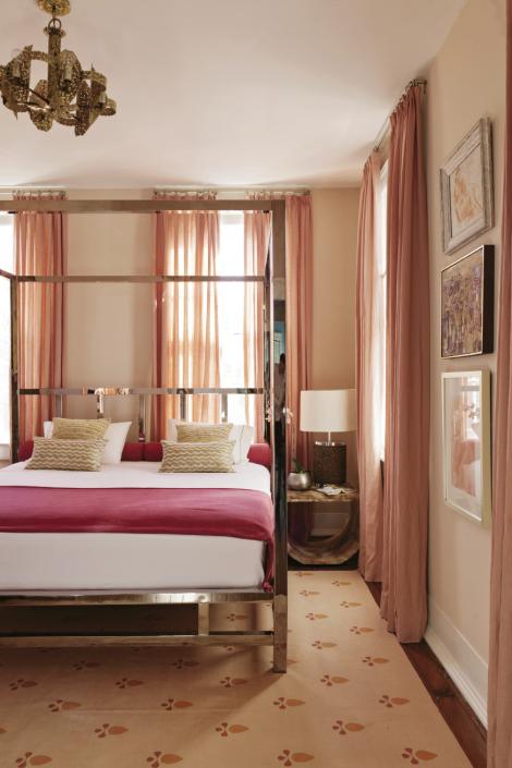 The chrome four-poster bed is custom, the U-shaped marbleized night table is by Baker, and the rug is by Madeline Weinrib. Sheer raspberry draperies echo the pale pink walls.