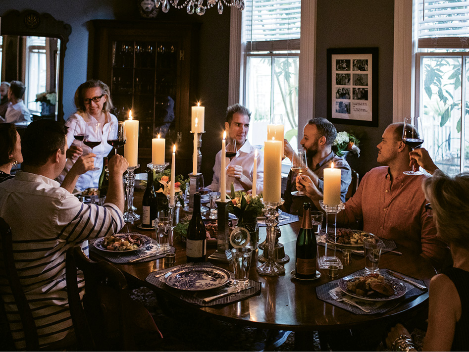 Friends raise glasses of wine around the candlelit table while Wagner gives a toast.