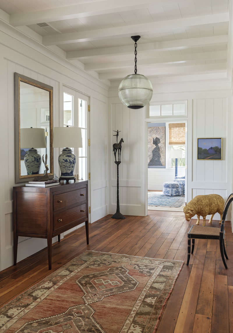 The large foyer provides an ideal space to showcase some of the couple’s sculptures, including  the bronze Horse and Rider II by Tom Corbin. A spectacular pair of Parisian street lamps repurposed into chandeliers hang in front of matching Holland MacRae Carlton chests. The layering of art and vintage rugs with blue and white porcelain lamps creates an inviting entrance.