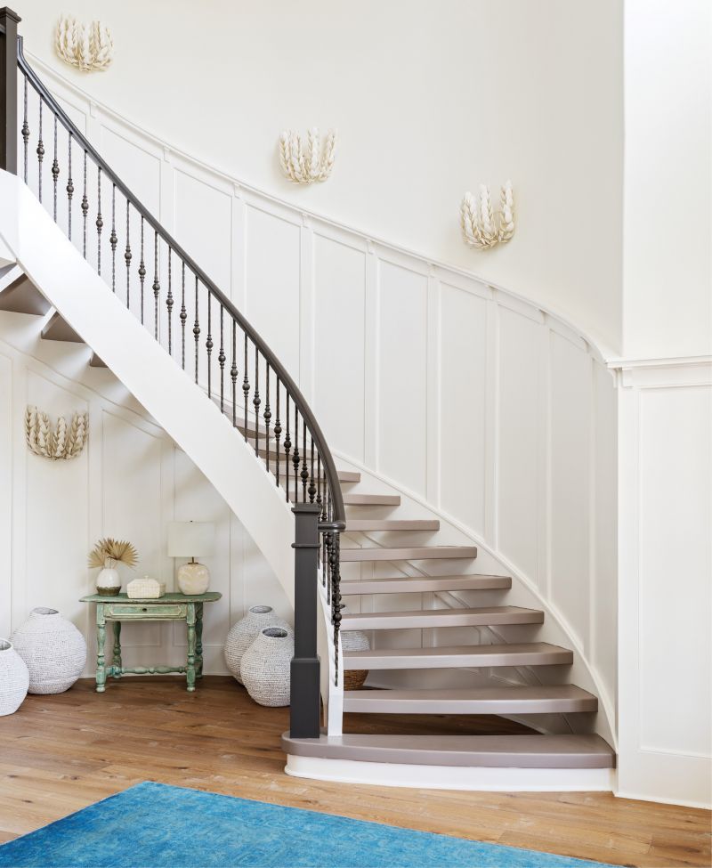 WELCOME IN: “It was a beautiful canvas to work with,” says interior designer Allison Elebash of the Leonard home, adding that its bones—including the foyer’s custom millwork and sweeping floating staircase—needed only cosmetic updates. She painted stair treads Farrow &amp; Ball’s “Charleston Charm” and installed white oak floors throughout the house to hide sand and fur. An azure rug from Antiques of South Windermere, seafoam-painted table from Acquisitions Interiors, woven jugs from GDC Home, and Palecek “Coco Magnolia” sconces (fashioned from hand-cut coconut shells) ground the space in its coastal locale.