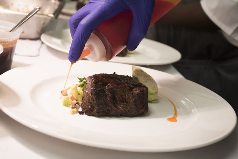A chef plates braised short rib with shrimp mousse and stuffed summer squash.