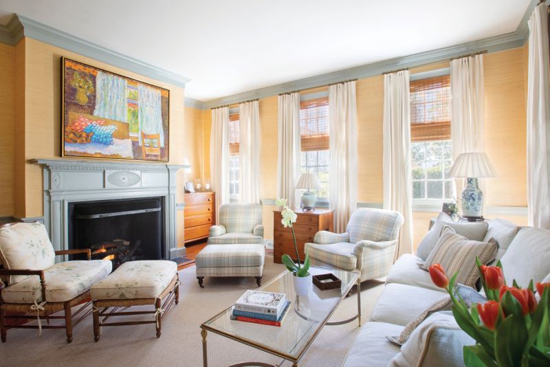 Peachy Keen: Caitlin designed the first-floor living room as a “palette cleanser” for the rest of the home, where bold colors and patterns dominate. The Thibaut “Pearl River”grasscloth wallpaper and white linen drapes provide a soft backdrop for the antique chests and French rush seat chair and ottoman. She had the original wood trim and hand-carved mantelpiece painted in Farrow &amp; Ball “Light Blue” to provide a subtle contrast.
