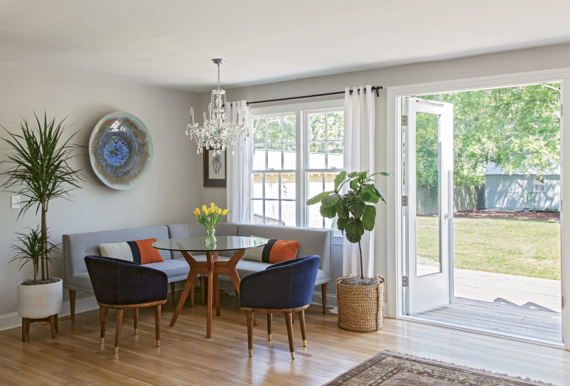 GATHER ’ROUND: Up to seven can fit comfortably in the West Elm-clad dining nook. When hosting a large group, Rachel simply swaps this glass tabletop out for a larger version. Pottery Barn drapes, a chandelier from Carolina Lanterns and Lighting, plants from Hyams, and a bowl hand-thrown by Louisiana artist Craig McMillan finish off the space.