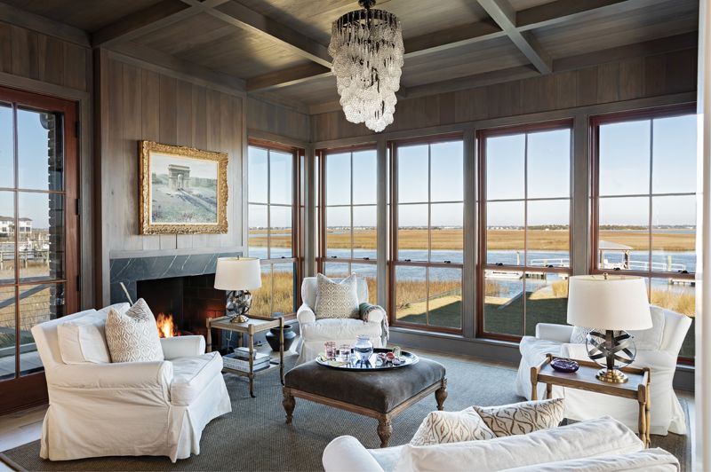 A Room With Three Views: The “coffee room” off the kitchen is the homeowner’s favorite spot. Paneled in custom-painted poplar, the luxurious space features a quartet of comfy chairs. A vintage glass chandelier complements the 19th-century painting of the Arc De Triomphe by Paul Gagni above the French limestone mantelpiece.