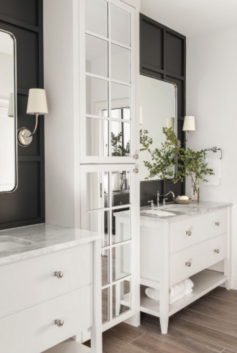 His &amp; Hers: Two vanities in the newly created en-suite bath for the primary bedroom continue the home’s black-and-white theme. Vendome sconces with white shades peek out from the black paneled walls and honed Carrara marble countertops on custom designed vanities are topped by nickel faucets from Water Street Brass.