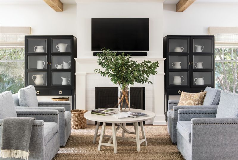 Shared Space: The open plan on the first floor uses the “rooms within a room” concept, sectioning the spacious area into three separate spaces through a combination of furniture and rugs. In the living room, the fireplace and television are the focal point, surrounded by custom furniture pieces sourced by Kristin. The couple refinished the existing custom cabinets and painted them in Benjamin Moore’s “Kendall Charcoal” to add a touch of drama.