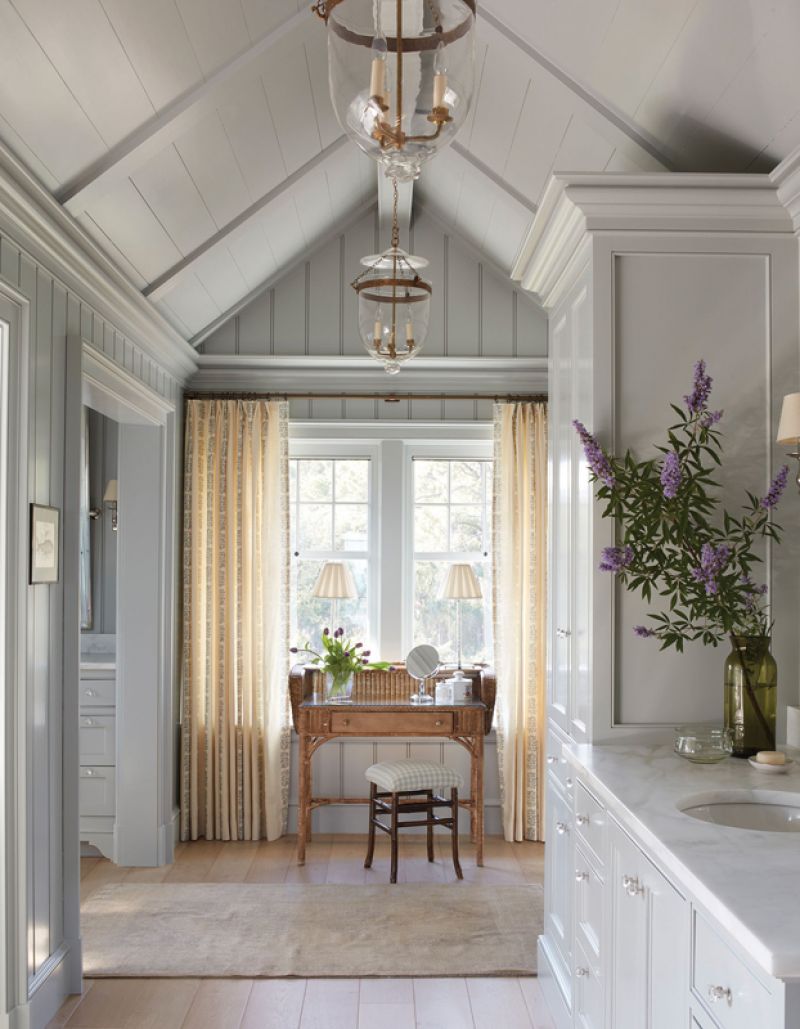 Soak It Up: The pale blue woodwork continues into the large primary bathroom suite, which is broken up into smaller spaces to create a more intimate feel. A dressing table from English Accent Antiques nestles at one end near a Keivan Woven Arts rug, complemented by Rose Tarlow drapes.